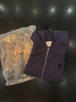 Ali Paris hoodie  - Snygg lila hoodie från Ami Paris med dragkedja framtill och klassisk huva med snören. På bröstet finns Ami:s Paris  ikoniska hjärta med A-broderi. Hoodien har känguruficka och ribbade muddar. Perfekt för en chill och trendig look.