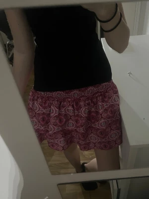 Kjol inbyggda shorts  - Säljer en rosa kortkjol med blommigt mönster och elastisk midja. Kjolen har en luftig och lätt form som passar perfekt till varma dagar. Köptes förra året på Plick 
