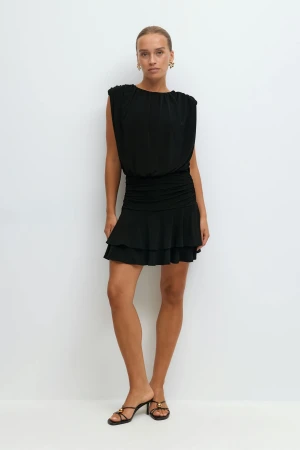 Svart volangklänning från Gina Tricot - Svart kort klänning från Gina Tricot med volangkjol och rynkade detaljer i midjan. Klänningen har en lösare passform upptill och är ärmlös med rund halsringning. Perfekt för dig som gillar en stilren och trendig look.
