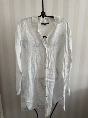 Vit långärmad linneskjorta - Säljer en vit långärmad skjorta i linne med klassisk krage och knappar framtill. Skjortan har en avslappnad passform och är perfekt för en stilren och enkel look. Passar lika bra till jeans som till shorts.