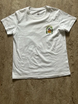 Vit t-shirt från Casablanca - Vit t-shirt från Casablanca med tryck på bröstet som föreställer en byggnad och texten 'Avenida Casablanca' i gult. Klassisk passform och rund halsringning. Perfekt för en stilren och avslappnad look.