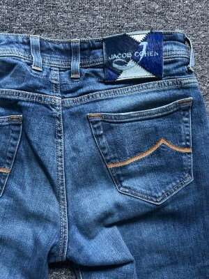 Blå jeans från Jacob Cohen - Snygga blå jeans från Jacob Cohen med klassisk femficksdesign och kontrastsömmar. Jeansen har en rak passform och är tillverkade i denim med en cool tvättad look. Perfekta för dig som gillar stilrena och tidlösa jeans.