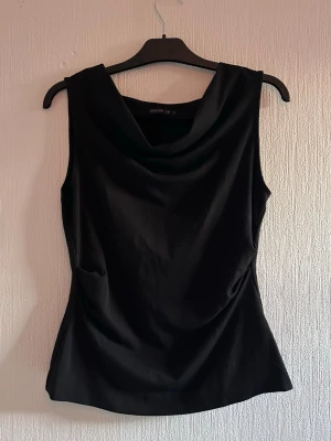Svart ärmlös topp från Stockh LM - Snygg svart ärmlös topp från Stockh LM med draperad halsringning. Toppen har en elegant och stilren design som passar perfekt till många olika outfits. Tillverkad i ett mjukt och följsamt material för en bekväm känsla.