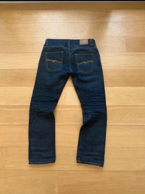 Mörkblå jeans från Nudie Jeans - Beskrivning  Säljer dessa Nudie Jeans i modellen Hank Rey Recycle Dry som inte längre produceras, och därmed ganska ovanliga. Modellen är en straight fit. Jeansen är tillverkade med Raw denim som fadear med tiden man använder dem. De är i otroligt bra skick med inga defekter och storlek är 32/32. Vid frågor eller funderingar är det bara att skriva (: Midja 45cm Benlängd 107cm( måtten är tagna av en amatör, finns chans att de är fel +-1 cm