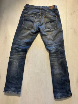 Blå jeans från Nudie Jeans - Snygga blå jeans från Nudie Jeans med klassisk femficksdesign och slitningar på benen. Jeansen har en rak passform och detaljerade sömmar på bakfickorna. Perfekta för en avslappnad och trendig stil.