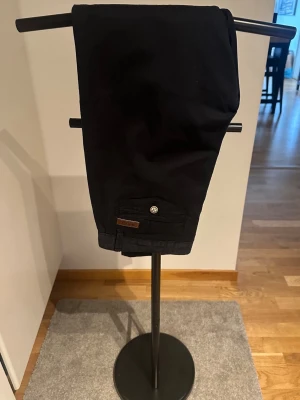 Marinblå chinos Indicode 32/32 - Snygga marinblå chinos från Indicode med klassisk rak passform och diskreta fickor fram och bak. Byxorna har bälteshällor och en liten logodetalj vid fickan. Perfekta för en stilren look och tillverkade i mjukt bomullstyg.