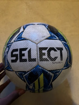 Select Samba fotboll storlek 5 - Säljer en Select Samba fotboll i storlek 5. Bollen är vit med blå, svarta och gula detaljer och har en klassisk design med tydliga paneler. Perfekt för träning eller match på gräsplan. Materialet är slitstarkt syntetiskt läder.
