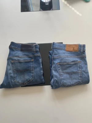 Två par blå jeans, olika tvättar - Säljer två par blå jeans i klassisk modell. Ena paret har slitningar och hål på låret för en trendig look, medan det andra är mer basic utan hål. Båda har fem fickor och skinnpatch bak i midjan. Perfekta till sneakers och hoodie.