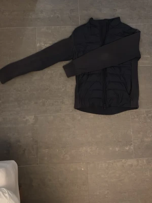 Svart cardiganjacka från Woolrich - Stilren svart cardiganjacka från Woolrich med quiltad framsida och stickade ärmar. Jackan har dragkedja framtill och ribbade muddar vid ärmslut och nederkant. Perfekt för sommar, vår och höst 