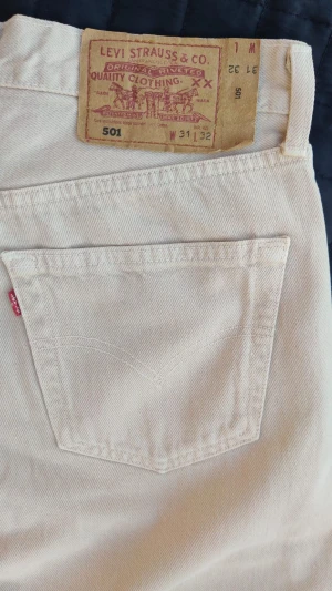 Levi's 501 beiga raka jeans collection - Säljer ett par klassiska beiga Levi's 501 jeans med rak passform och femficksdesign. Jeansen har den ikoniska läderpatchen bak i midjan och röd Levi's-tagg på bakfickan. Tillverkade i kraftig denim, perfekta för en clean och tidlös look. 