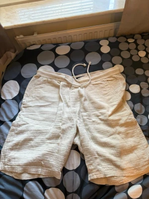 Beiga shorts med snörning - Snygga beiga shorts i mjukt material med avslappnad passform och snörning i midjan. Perfekta för varma dagar och enkel att matcha med t-shirt eller linne.