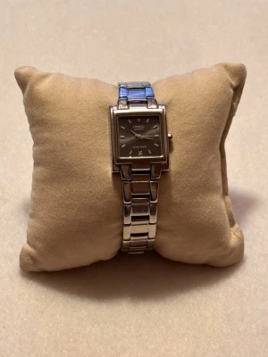 Casio silverfärgad fyrkantig klocka - Stilren klocka från Casio med fyrkantig urtavla och länkarmband i silverfärgad metall. Urtavlan är mörk med minimalistiska markeringar och diskret logga. Perfekt accessoar för dig som gillar klassisk och tidlös design.