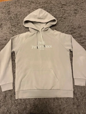 Ljusgrå hoodie Peak Performance - Snygg ljusgrå hoodie från Peak Performance med klassisk logga tryckt på bröstet. Hoodien har huva med dragsko, magficka och ribbade muddar vid ärmar och nederkant. Perfekt för en avslappnad och stilren look. Står att det är storlek M men skulle mer säga att den passar S. Vänligen mät så du ser att den passar (de två sista bilderna). Kom gärna med prisförslag!🤩