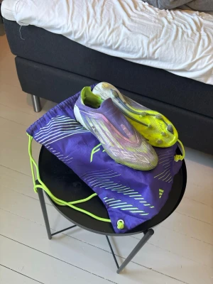 Adidas f50 laceless elite - Säljer ett par snygga fotbollsskor i lila och gult med modern design och låg vikt. Skorna har dobbar för spel på gräs och kommer med en matchande lila påse med neonfärgade detaljer. Perfekta för dig som vill sticka ut på planen.