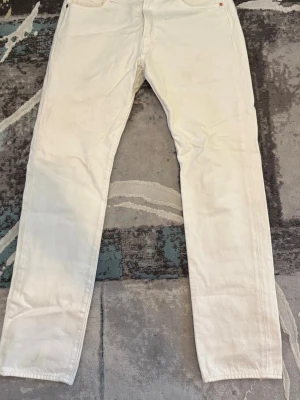 Cream white 501 jeans från Levi's - Säljer ett par vita 501 jeans från Levi's med rak passform och klassisk femficksdesign. Jeansen har Levi's ikoniska läderpatch bak i midjan och röd logotagg på bakfickan. Tillverkade i kraftig denim som ger en clean och stilren look. Endast använd 2 gånger.