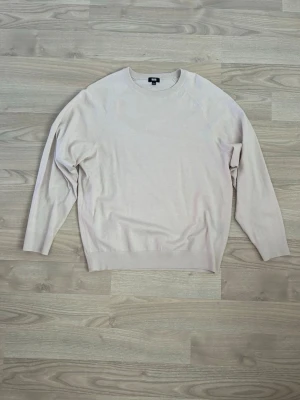 Ljusbeige stickad tröja - En stilren ljusbeige stickad tröja med rund halsringning och långa ärmar. Tröjan har en enkel design utan synliga detaljer eller mönster och är tillverkad i ett tunt, mjukt material som passar perfekt till lager på lager.