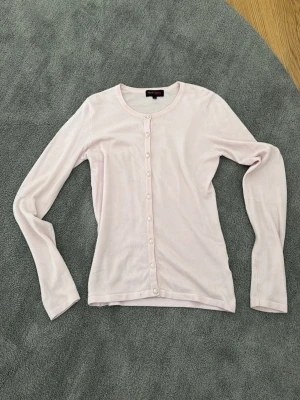 Ljusrosa kofta från MaxMara - Söt ljusrosa kofta från MaxMara med rund halsringning och knappar framtill. Långärmad och i tunt, mjukt material som känns skönt mot huden. Perfekt att slänga över en topp för en enkel men stilren look.