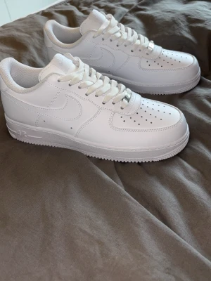 Airforce  - Säljer ett par helvita Nike airforce  sneakers i läder med ikonisk swoosh på sidan och perforerade detaljer på tån. Skorna har vita snören och en tjock sula med AIR-detalj. Perfekta för dig som gillar stilrena och tidlösa sneakers.