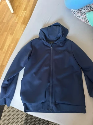 Mörkblå hoodie med dragkedja - Snygg mörkblå hoodie från McKenzie med dragkedja framtill och huva. Tillverkad i ett mjukt och stretchigt material som passar perfekt för en avslappnad stil. Diskret logga på bröstet och ribbade muddar vid ärmslut och nederkant.