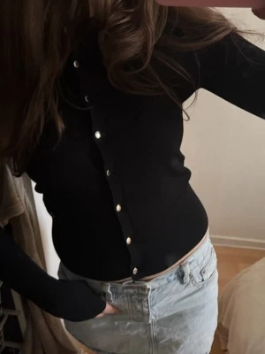 Svart ribbad cardigan med knappar - Snygg svart ribbad cardigan med långa ärmar och silverfärgade knappar framtill. Figurnära passform och mjukt material som känns skönt mot huden. Perfekt att styla med jeans eller kjol för en clean look.