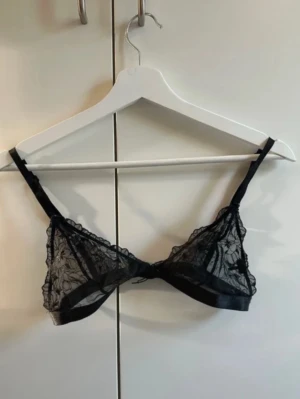 Svart spets-bh med blommönster - Säljer en svart bh i transparent spets med fina broderade blommor. Bh:n har tunna, justerbara axelband och ingen vaddering eller bygel. Perfekt för dig som gillar en lätt och luftig känsla. Materialet är mjukt och följsamt.