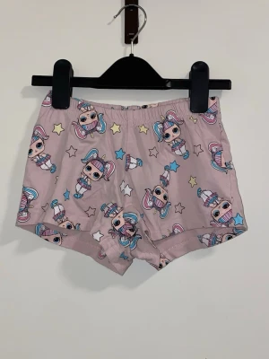 Rosa kalsonger med LOL Surprise-motiv - Säljer ett par rosa kalsonger med gulligt LOL Surprise-tryck och stjärnor i olika färger. Modellen är boxershorts med resår i midjan och mjukt material, perfekt för dig som gillar färgglada och lekfulla underkläder.