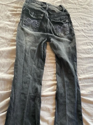 Svarta bootcut jeans med broderi - Säljer ett par svarta bootcut jeans med snyggt vitt broderi på bakfickorna. Jeansen har klassisk femficksmodell och dragkedja fram. Materialet är denim med lätt tvättad look och raka ben. Perfekta för dig som gillar en avslappnad men ändå trendig stil.