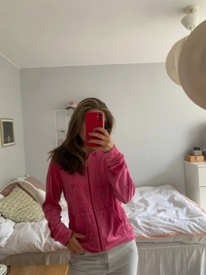 Rosa velour hoodie från Twilfit - Säljer en ikonisk rosa velour hoodie från Twilfit med dragkedja framtill och två fickor. Hoodien har huva med snören och guldfärgade detaljer. Perfekt för en chill och trendig look, supermjuk och skön att ha på sig. 