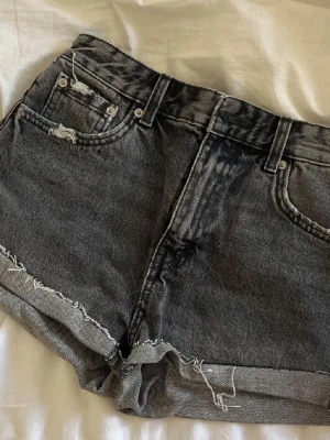 Grå jeansshorts - Säljer ett par grå jeansshorts i klassisk femficksmodell. Shortsen har fransiga kanter och lite slitna detaljer både fram och bak. Perfekta till sommaren och lätta att matcha med allt.