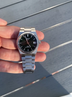 Tissot PRX Powermatic 80 klocka - Säljer en stilren Tissot PRX Powermatic 80 med blå urtavla och datumfönster. Klockan har ett klassiskt armband i borstat stål och en rund boett med raka linjer. Perfekt för dig som gillar tidlös design och schweizisk kvalitet.