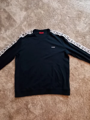 HUGO SWEATSHIRT - XL - Mörkblå sweatshirt från HUGO med vita logoband längs ärmarna och diskret HUGO-tryck på bröstet.   Toppskick!