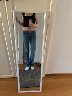 Blå bootcut jeans med låg midja - Säljer ett par klassiska blå bootcut jeans med låg midja och fem fickor. Jeansen har en enkel design utan slitningar och är gjorda i ett mjukt denimtyg som sitter snyggt på benen. Perfekta till crop tops eller hoodies. står inte vilken storlek vad jag sett men passar som s/36.