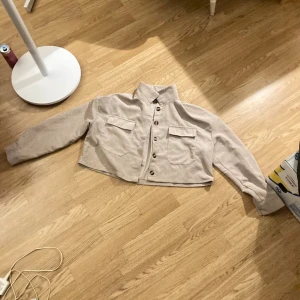 Beige croppad manchester jacka - Säljer en stilren beige croppad manchester jacka i storlek M. Med raka ärmar och stora bröstfickor(riktiga). Den har knappar framtill och är endast testad. Säljes pga att jag tycker den är för kort🤩☺️