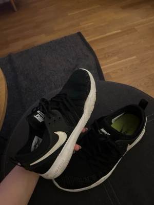 Svarta Nike sneakers med vit sula - Svarta sneakers från Nike med vit sula och vit swoosh-logga på sidan. Skorna har lågt skaft, snörning och ovandel i mesh och syntetmaterial för en sportig look. Perfekta för en avslappnad och trendig stil.