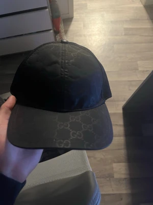 äkta gucci nylon keps - Snygg svart keps från Gucci med det klassiska GG-mönstret på både skärmen och framsidan. Kepsen har mesh på sidorna för extra ventilation och en böjd skärm. Perfekt accessoar för en trendig och avslappnad stil.