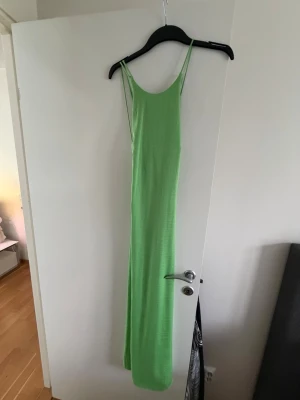 Grön långklänning med smala band - Snygg grön långklänning med smala axelband och snörning i ryggen. Klänningen har en rak passform och är tillverkad i ett lätt material som passar perfekt till varma dagar. Enkel och stilren design som känns modern och fräsch.