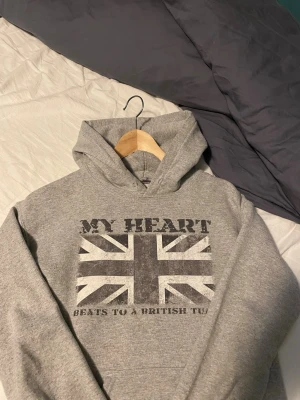Grå hoodie med brittiskt tryck Gildan - Snygg grå hoodie från Gildan med tryck av den brittiska flaggan insydd själva för att den ska ha en tightare form vilket den har men den håller på att gå upp så kan va nåt hål kan skicka bild privat vid köp om det behövs 😀