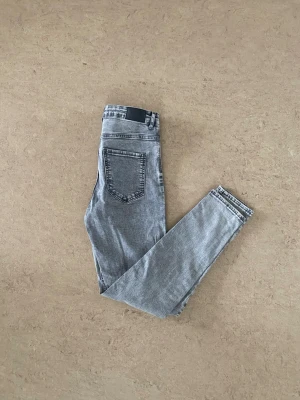 Grå skinny jeans från Perfect Jeans - Säljer ett par grå skinny jeans från Perfect Jeans med klassisk femficksdesign och svarta detaljer på bakfickan. Jeansen har en smal passform och är tillverkade i stretchigt material för extra komfort. Perfekta till en avslappnad streetstyle-look.