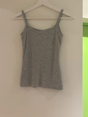 Grå ribbad linnetopp - Säljer en enkel och stilren grå ribbad linnetopp med smala axelband. Perfekt att matcha med jeans eller kjol för en avslappnad look. Materialet är mjukt och stretchigt för extra komfort.