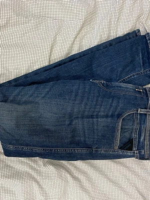 Mörkblå jeans från Replay - Säljer ett par mörkblå jeans från Replay med klassisk femficksmodell och snygga slitningar. Jeansen har raka ben och detaljerade sömmar. Perfekta för dig som gillar en tidlös och avslappnad stil.