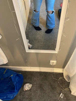 Ljusblå bootcut jeans med slitningar - Säljer ett par ljusblå bootcut jeans med stora slitningar vid knäna. Jeansen har hög midja och klassiska fem fickor. Materialet är denim med en skön stretch. Perfekta för dig som gillar en avslappnad och trendig stil.