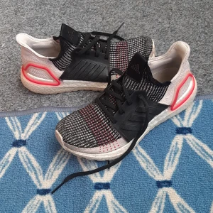 Adidas löparskor med svart och vit ovandel - Säljer ett par Adidas sneakers med stickad ovandel i svart, vitt och röda detaljer. Skorna har snörning, vit sula och svarta tre ränder på sidan. Perfekta för träning eller vardag. skoSkor är mycket lätta och bekväma i mycket bra skick. 