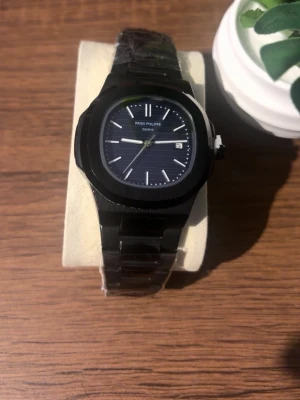 Klocka  - Stilren svart klocka med mörk urtavla och tydliga vita markeringar. Klockan har datumvisning och en klassisk länk i metall. Perfekt accessoar för dig som gillar exklusiv och tidlös design. Priset kan diskuteras!