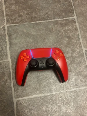 Röd PlayStation 5 DualSense kontroll - Säljer en röd och svart PlayStation 5 DualSense handkontroll från Sony. Kontrollen har en snygg design med röda knappar. Säljer den då jag inte använder den längre. Den funkar som den ska