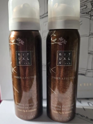 Rituals, Under a Fig Tree " 25 years celebration collection" - Två flaskor Rituals foaming shower gel i doften Under a Fig Tree. Flaskorna är bronsfärgade med vita blommönster och har en praktisk vit plastkork. Moussen har en fräsch doft av fikon och copaiba, perfekt för en lyxig duschupplevelse.