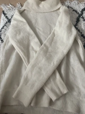 Vit polotröja från STOCKH LM - Mysig vit stickad polotröja från STOCKH LM i storlek M. Tröjan har långa ärmar, ribbstickade muddar och hög polokrage. Perfekt för kalla dagar och enkel att matcha med olika outfits. Smutsvit