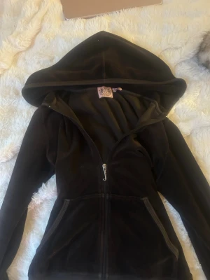 Brun juicy couture  med dragkedja - Mjuk och skön brun hoodie i velour från Juicy Couture. Hoodien har dragkedja framtill, stor huva och två fickor. Perfekt för en avslappnad och trendig look. Klassisk passform och ikonisk logga på etiketten i nacken. Storlek M men passar S bättre.