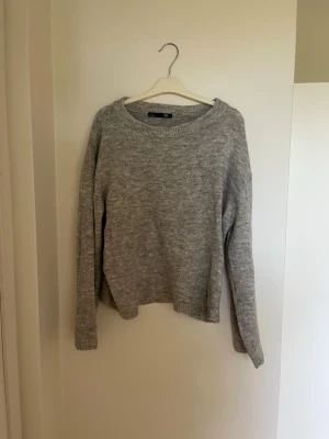Grå stickad tröja i enkel design - Mysig grå stickad tröja med rund halsringning och långa ärmar. Tröjan har en avslappnad passform och ribbstickade muddar vid ärmslut och nederkant. Perfekt för lager på lager och vardagsstil.