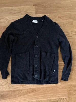 Lindbergh Cardigan i Ull - Lindbergh Cardigan i Ull och den har en fin mörkgrå/svart färg. Priset ej hugget i sten. Hör av vid funderingar!