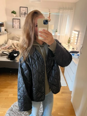 Svart quiltad dunjacka - Stilren svart dunjacka med quiltat mönster och oversized passform. Jackan har dragkedja framtill och rundad nederkant. Tillverkad i glansigt material som ger en modern look. Perfekt för dig som vill ha en lätt och trendig jacka till vintern.